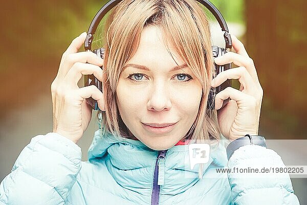 Nahaufnahme Porträt einer schönen jungen Frau mit Kopfhörern  die draußen im Wald Musik hört. Fröhliche Musik