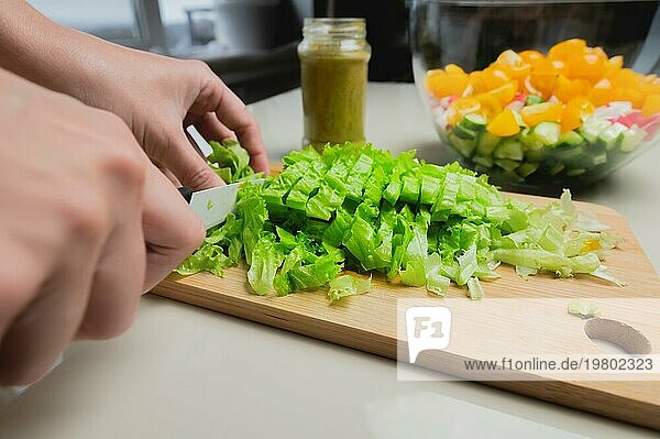 Weibliche Hände schneiden Salatblätter mit einem Messer vor dem Hintergrund einer Schüssel mit gehacktem Gemüse. Vegetarisches Essen Vorbereitung
