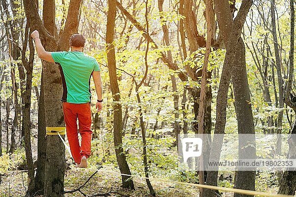 Rückansicht bärtiger Mann im Alter geht an einem sonnigen Nachmittag im Herbstwald an einer Slackline entlang. Das Konzept der Freizeit und Erholung von aktiven Menschen mittleren Alters