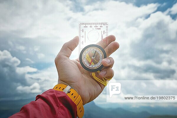 Männliche Hand hält einen magnetischen Kompass auf dem Hintergrund des Himmels mit Wolken. Das Konzept des Reisens und der Suche nach dem eigenen Lebensweg