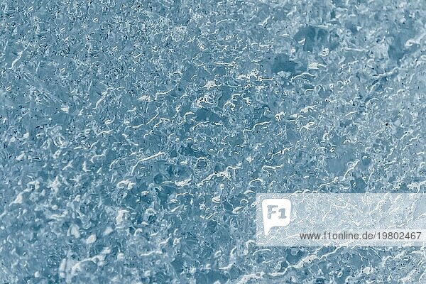 Nahaufnahme der Oberfläche eines Gletscherfragments mit einer Struktur aus Streifen und Blasen. Eisblaue Textur im Licht. Kleine Schärfentiefe