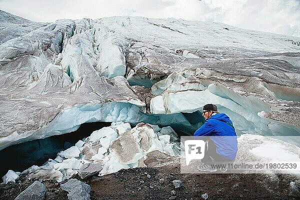 Der Reisende mit Mütze und Sonnenbrille sitzt in den verschneiten Bergen auf dem Gletscher. Reisender in einer natürlichen Umgebung