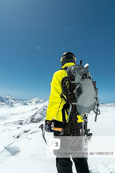 Ein Bergsteiger hält einen Eispickel hoch in den schneebedeckten Bergen. Blick von hinten. outdoor extrem outdoor klettern sport mit Bergsteigerausrüstung