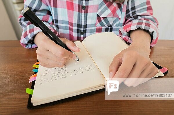 Junge kaukasische attraktive Frau macht sich Notizen in ihrem Notizbuch  während sie in der Küche am Tisch sitzt. Papier Notebook schreiben weibliche Hände