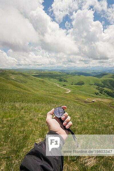 Männliche Hand eines Touristen mit einem echten Kompass vor dem Hintergrund einer Berglandschaft