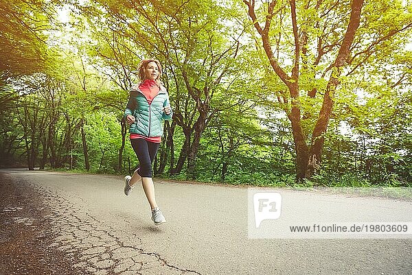 Junge Fitness blonde Frau mit Kopfhörern laufen am Morgen kaukasischen Waldweg in der Sonne Licht