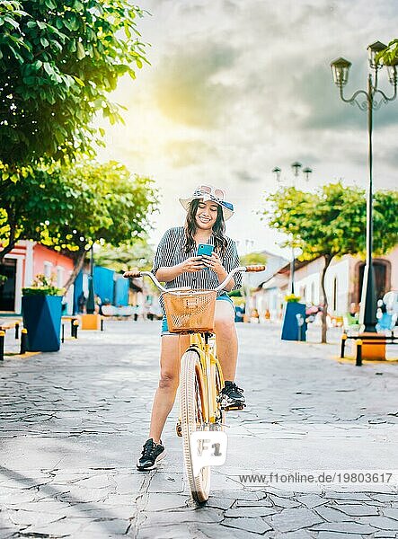 Happy Tourist Mädchen auf dem Fahrrad mit Handy auf der Straße. Schönes Mädchen in Hut auf Fahrrad mit Handy auf der Straße von La Calzada  Granada  Nicaragua  Mittelamerika