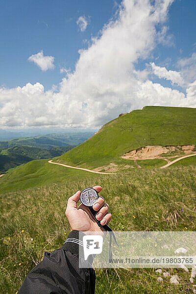 Ein Mann die Hand eines Touristen mit einem authentischen Kompass auf dem Hintergrund einer Bergstraße Landschaft