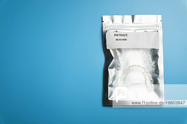 Eine silberne Tasche mit einem weißen Etikett  in der sich 3D gedruckte Aligner befinden. blaür Hintergrund  Studioaufnahme