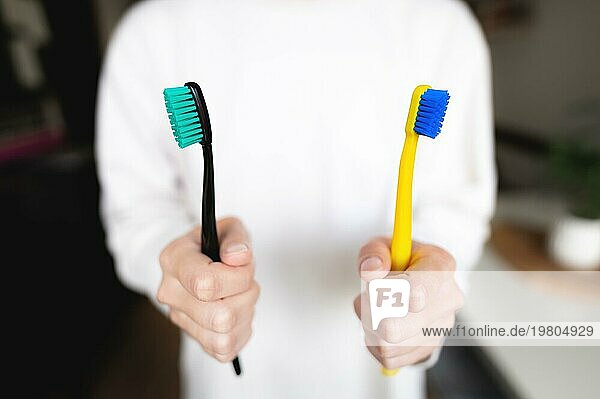 Die Hand einer Frau hält zwei Zahnbürsten. Zahnärztliche Richtung  das Thema der morgendlichen Hygiene eines Ehepaares