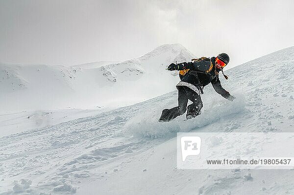 Snowboarderin  eine junge Frau in Bewegung auf einem Snowboard in den Bergen in einem Freeride nicht weit von der Skipiste  macht einen Abfahrtslauf