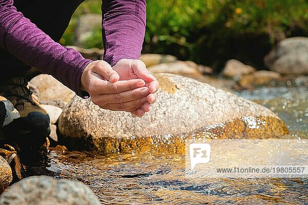 Frauenhände in Nahaufnahme schöpfen Wasser aus einem Gebirgsbach  um den Durst zu löschen  trinken aus einer sauberen Wasserquelle. Touristen an einem heißen sonnigen Tag