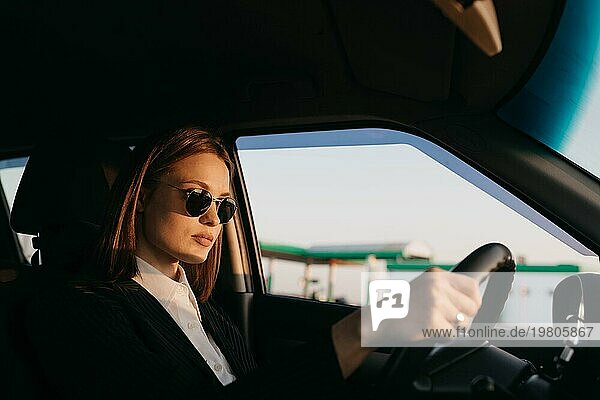 Junge schöne stilvolle Mädchen Fahrer in einer Jacke und Sonnenbrille fahren ein Auto  Geschäftsreise