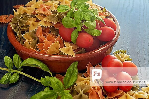 Schüssel mit Nudeln  frischen Tomaten und Basilikumblättern  Zutaten für die italienische Küche  Nudeln in Bogenform