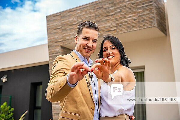 Frontale Nahaufnahme eines lächelnden Paares  das ein neues Haus kauft und die Schlüssel zeigt