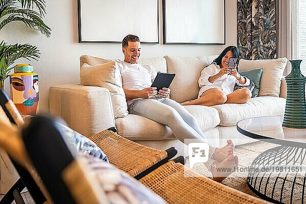 Technologisches Wochenende für ein Paar in legerer  bequemer Kleidung auf dem Sofa