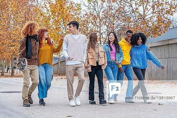 Multiethnische Freunde plaudern und schlendern an einem Herbsttag entspannt die Straße entlang