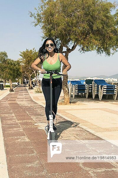 Junge Latina Frau mit Spaß mit elektrischen Roller am Strand