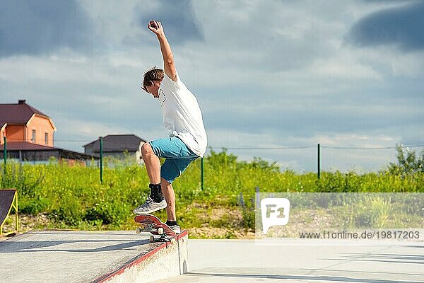 Junge Skateboarder in einem Skatepark  der einen Ollie Trick auf einem Skateboard vor einem Himmel und Gewitterwolken macht