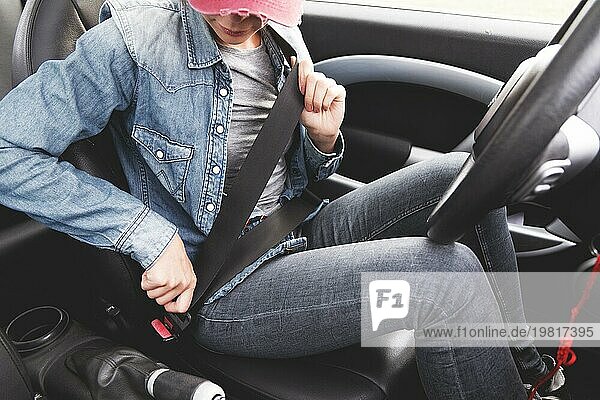 Ein Hipster Mädchen in Jeanskleidung schnallt sich im Auto an. Vorstellung von sicherem Fahren