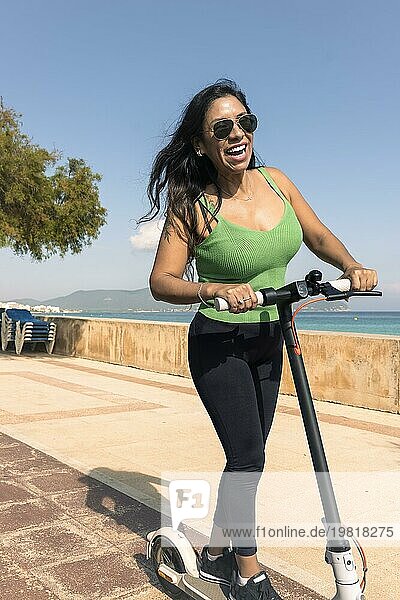 Junge Latina hat Spaß mit einem Elektroroller auf der Strandpromenade