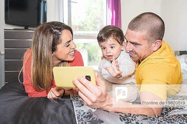 Eltern und kleiner Junge  der ein Mobiltelefon benutzt  liegen zusammen auf dem Bett
