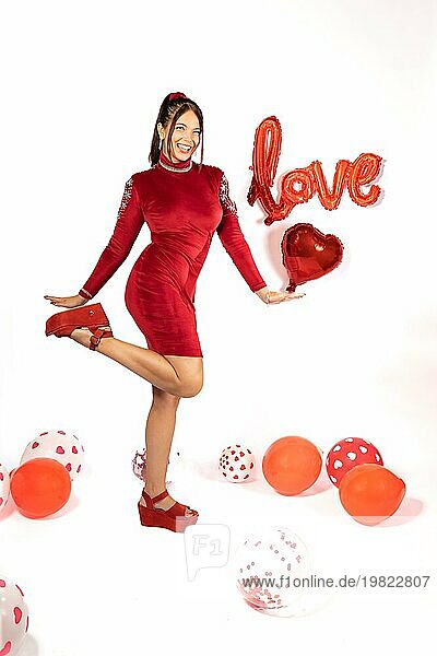 Schöne junge Latina Frau in rotem Kleid stehend schaut und lächelt in die Kamera  umgeben von Luftballons auf weißem Hintergrund mit Liebe Zeichen. Valentinstag Konzept