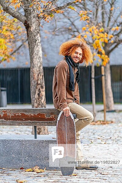 Vertikales Porträt der Seitenansicht eines alternativen erwachsenen Mannes mit einem Skateboard in einem Stadtpark im Herbst