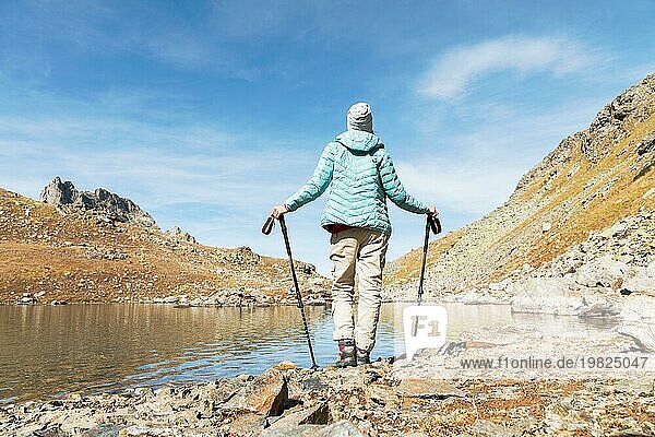 Eine schlanke Rucksacktouristin mit Wanderstöcken steht neben einem Hochgebirgssee hoch in den Bergen des Kaukasus. Ein Rahmen für das Leben. Das Konzept der freien Zeit in den Bergen an der frischen Luft