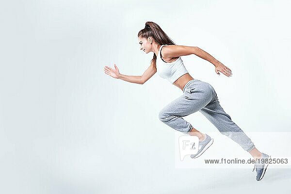 Sportliche Läuferin auf weißem Hintergrund. Foto einer attraktiven Frau in modischer Sportkleidung. Dynamische Bewegung. Seitenansicht. Sport und gesunder Lebensstil. Gemischte Medien