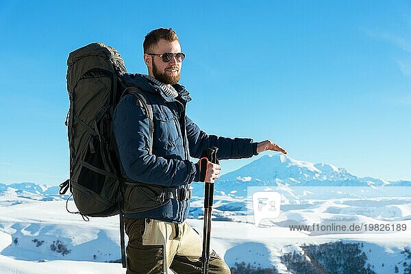 Ein Hipster Reisender mit Bart und Sonnenbrille in der Natur. Ein Mann wandern in den Bergen mit einem Rucksack und skandinavischen Wanderstöcke im Hintergrund eines Berges Elbrus Landschaft und blaün Himmel. Reisen Lifestyle Abenteuer Outdoor Erholung übertreffen