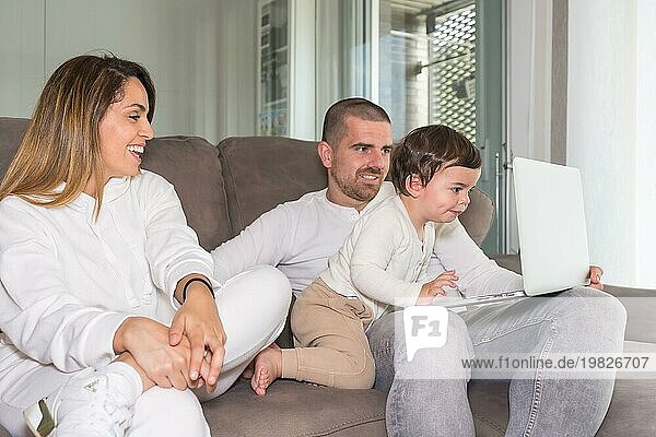 Familie mit Laptop und Baby  die zusammen auf dem Sofa sitzen