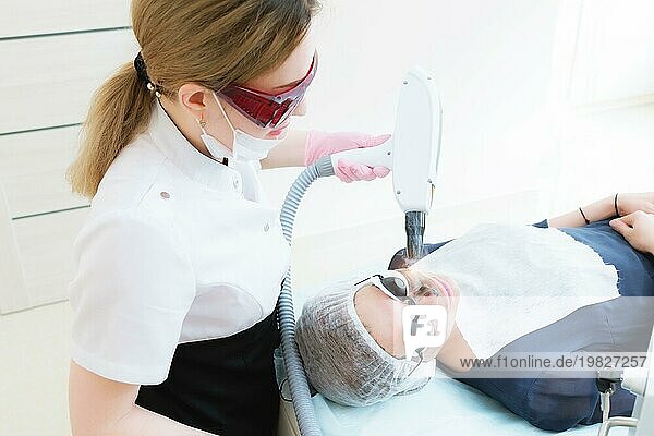 Die Kosmetikerin mit Schutzbrille führt das Verfahren des Carbon Peelings mit Hilfe eines kosmetologischen Lasers durch. Carbon Gesichtspeeling Verfahren. Die Laserimpulse reinigen die Gesichtshaut. Hardware Kosmetologie Behandlung. Prozess der Photothermolyse  Erwärmung der Haut