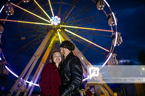 Verliebtes Paar in einem Vergnügungspark in der Nähe eines Riesenrads bei einer Verabredung bei kaltem Wetter. Das Konzept von Liebe und Freude in Beziehungen