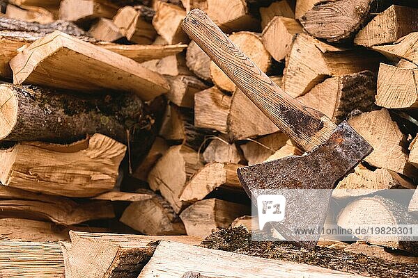 Die Axt steckt in einem Baumstamm vor dem Hintergrund von gehacktem Brennholz  das auf einem flachen Stapel liegt. Nahaufnahme