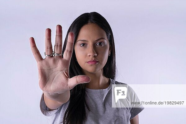 Junge lateinische Frau in lässigem Outfit macht die Hand Stoppschild gegen lila Studio Hintergrund. Konzept Frauentag