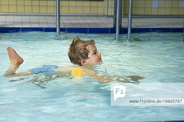Topic: Preschool child with swimming noodle in swimming pool learns to swim in a public pool