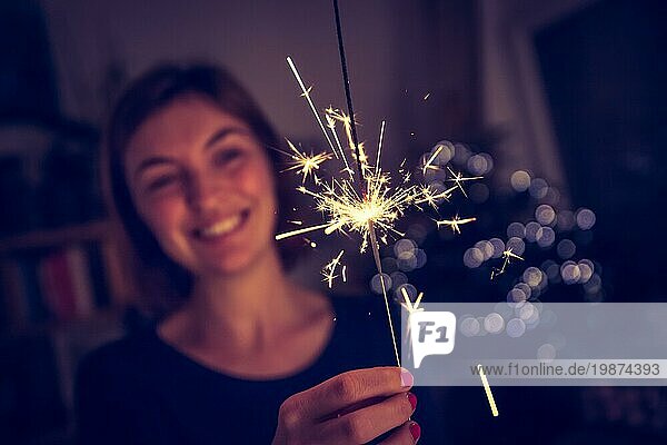 Lächelndes Mädchen hält eine Wunderkerze in der Hand  innen  Lichter im Hintergrund