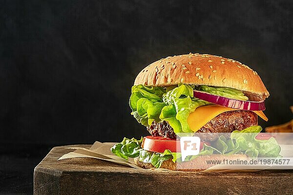 Burger mit Rindfleisch  Käse  Zwiebel  Tomate und grünem Salat  eine Seitenansicht auf einem dunklen Hintergrund mit Kopierraum