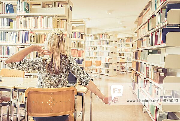 Müde Studentin sitzt am Schreibtisch mit Stapel von Büchern  Universitätsbibliothek