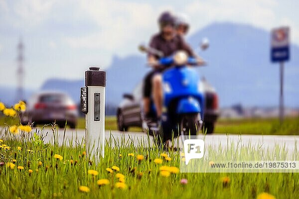 Leitpfosten und ein Paar auf einem Motorrad an einer idyllischen asphaltierten Straße im Sommer  Blumen und grünes Gras