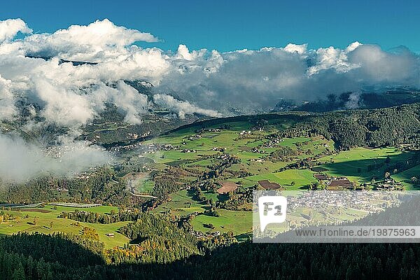Panoramablick von einem Berg auf das Dorf Ums  Völs am Schlern  in den italienischen Alpen an einem sonnigen Tag mit dichten weißen Wolken  die über dem Tal schweben
