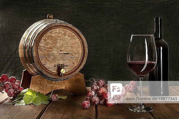 Ein Glas Rotwein mit einer Flasche  ein Weinfass  Trauben und Weinblätter  auf einem dunklen rustikalen Hintergrund  Low Key Foto mit einem Platz für Text