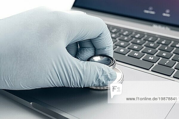 Hand hält ein Stethoskop auf einem modernen Laptop Computer. Konzept eines Technikers  der Computerprobleme überprüft
