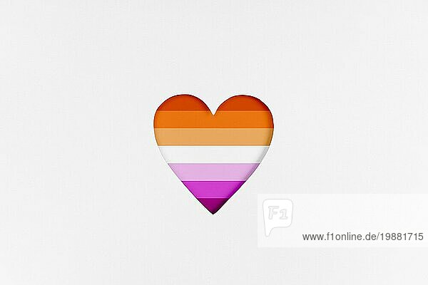 Lesbische Flagge auf Herzform vor weißem Hintergrundem Karton Hintergrund. Bedruckter Karton mit ausgestanzter Herzform. Ansicht von oben