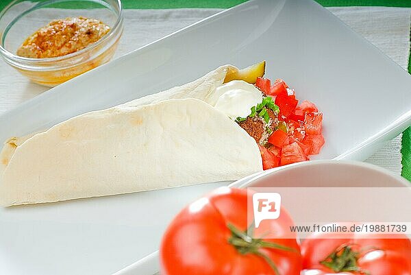 Frischer traditioneller Falafel Wrap auf Fladenbrot mit frischen gehackten Tomaten  Foodfotografie