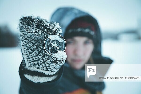 Junge Frau hält einen Kompass hoch. Winterzeit  Handschuhe und Kapuze
