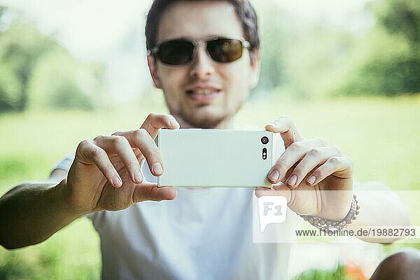 Mann macht ein Foto mit seinem Handy  draußen im Park