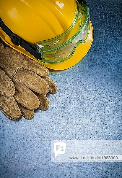 Vertikale Ansicht von schützenden Lederhandschuhen  gelbem Bauhelm und Plastikschutzbrille auf zerkratztem metallischem Hintergrund Baukonzept