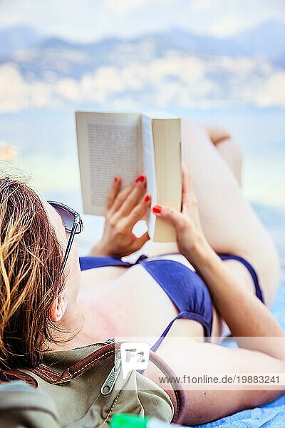 Junge schöne Frau im Bikini liest ein Buch am Strand